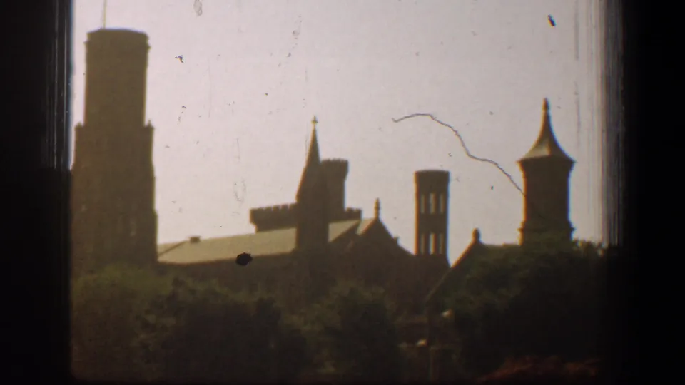 Distant Washington, DC cathedral roofline with towers and spires seen above trees in warm, faded 1961 8mm color.