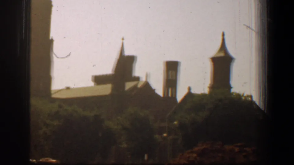 Final 1961 Washington, DC frame showing cathedral towers and spires behind trees, with dust, scratches, and dark 8mm frame edges.