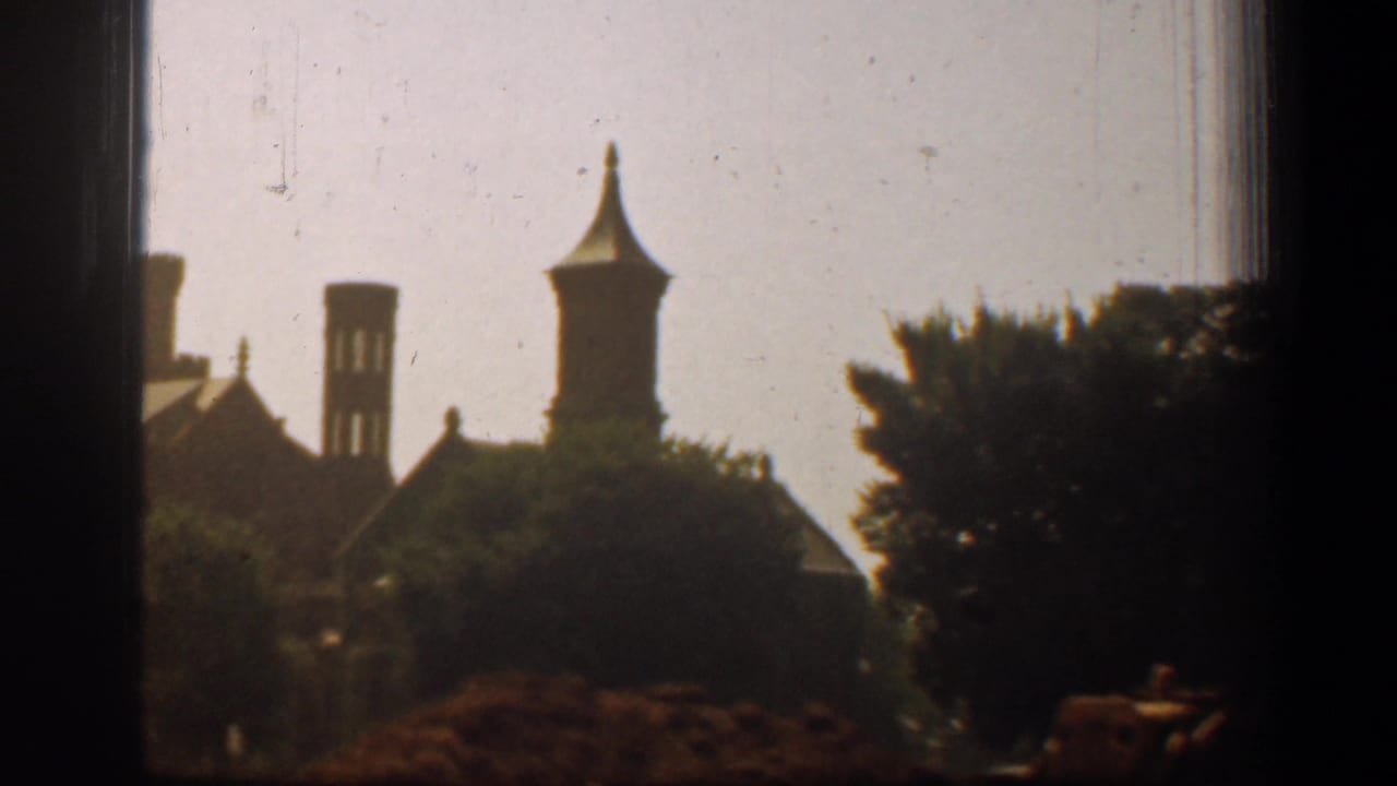 1961 home-movie view from a vehicle window showing distant Washington, DC building silhouettes, trees, and soft 8mm film grain.