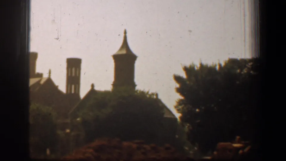 1961 home-movie view from a vehicle window showing distant Washington, DC building silhouettes, trees, and soft 8mm film grain.