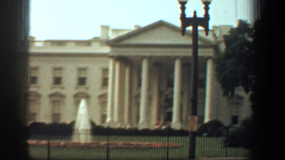 The White House facade appears beyond the front fence, framed by trees and a streetlamp in 1961 8mm footage.