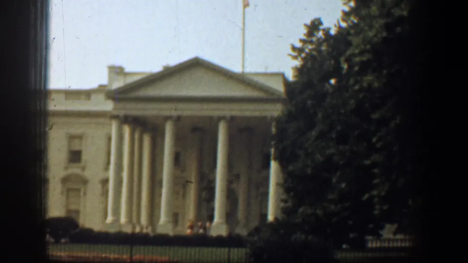 A closer 1961 8mm view centers the White House portico, columns, flagpole, fence, and nearby tree cover.