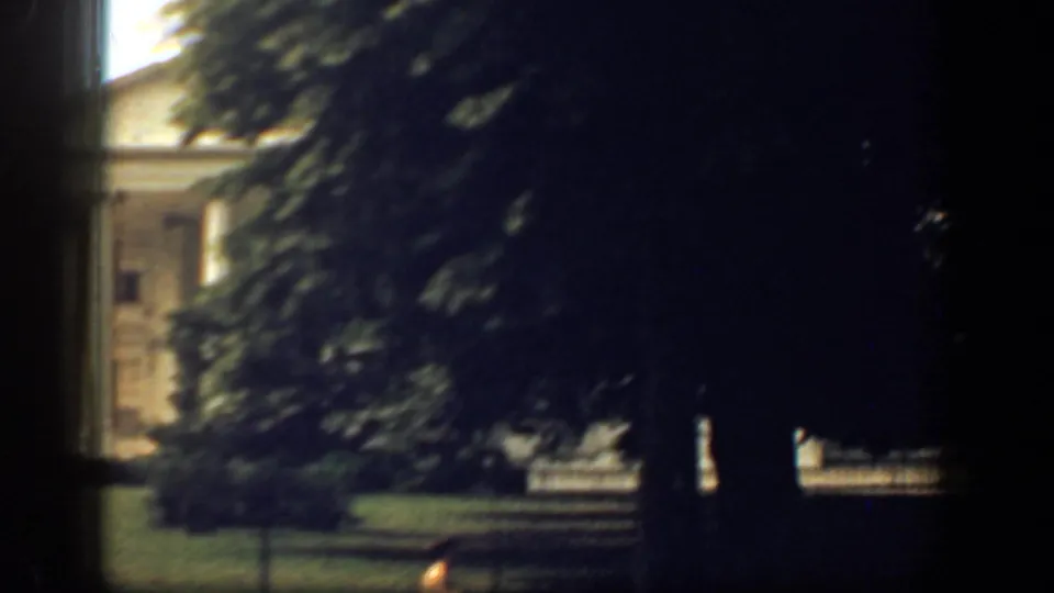 A shadowed 1961 Washington DC frame shows trees partly blocking the White House and grounds in soft 8mm focus.