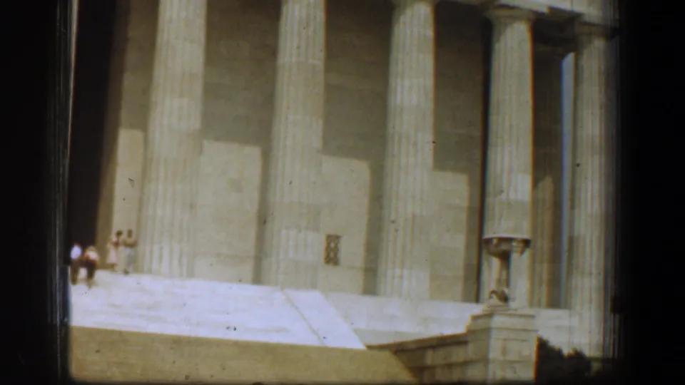 Home-movie frame of the Lincoln Memorial steps, columns, and distant visitors, partly bordered by dark film edges.