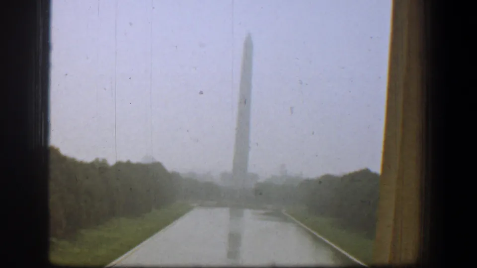 1961 Washington, DC view through a window toward the Washington Monument, with wet pavement and trees under overcast light.