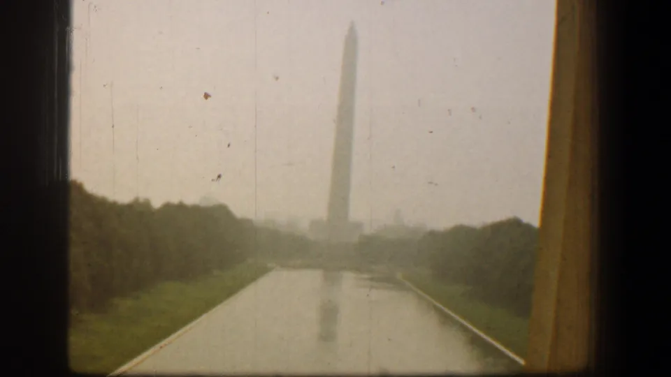 1961 Washington, DC view of the Washington Monument and its reflection across the Reflecting Pool, partially framed by a dark window edge.