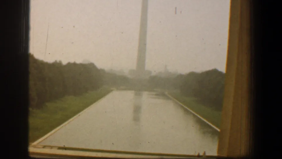 1961 Washington, DC home-movie frame showing the Washington Monument over the Reflecting Pool, bordered by window and curtain edges.