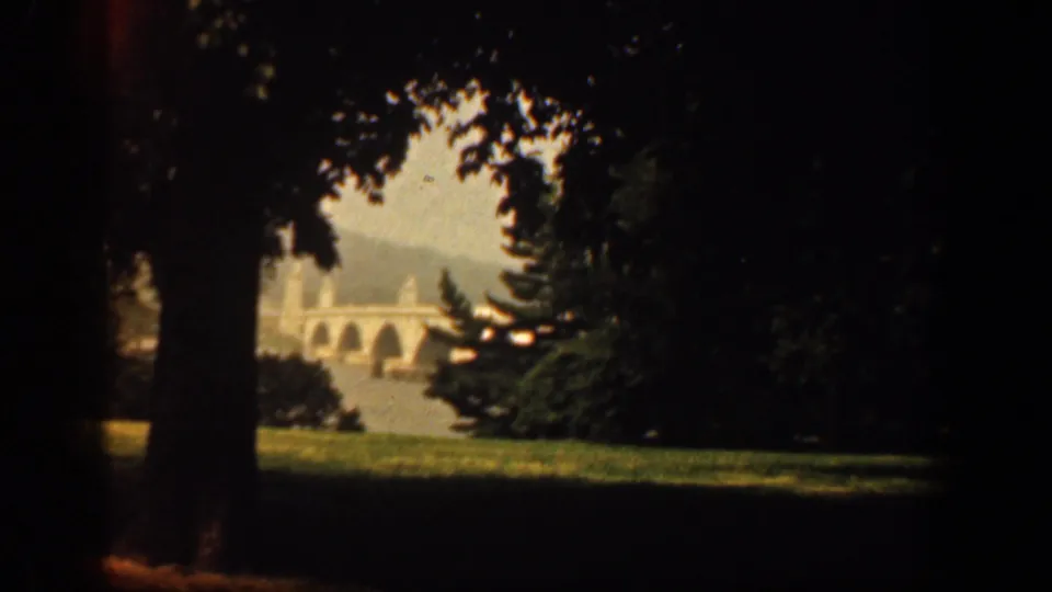 Scenic Washington DC home-movie view from 1961, showing a distant arched stone bridge or structure through trees and lawn.