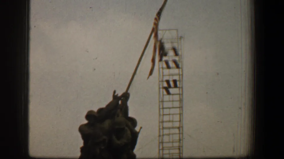 1961 8mm frame of the Marine Corps War Memorial from below, with the soldier figures, American flag, and scaffold tower clearly visible.