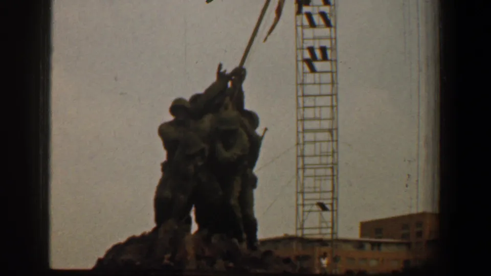 The Iwo Jima Memorial appears in a soft 8mm frame, with the flagpole angled upward and a tall crane visible to the right.