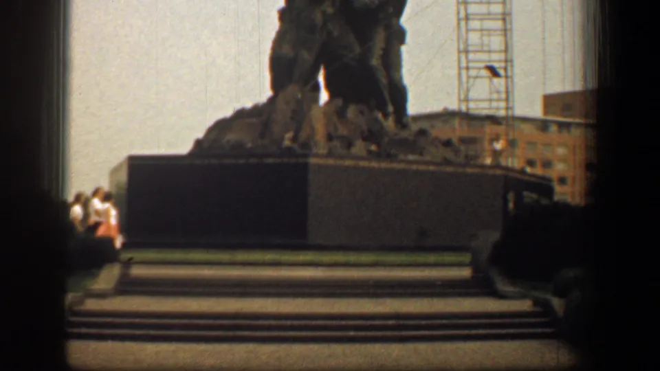 1961 Washington, DC frame with the war memorial sculpture cropped high, broad pedestal and steps visible, and small visitors standing near the base.