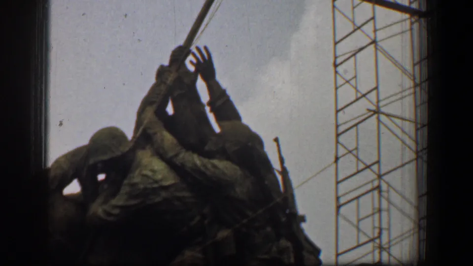 Close 1961 8mm view of the flag-raising soldier sculpture in Washington, DC, with a tall construction crane and pale sky in the background.
