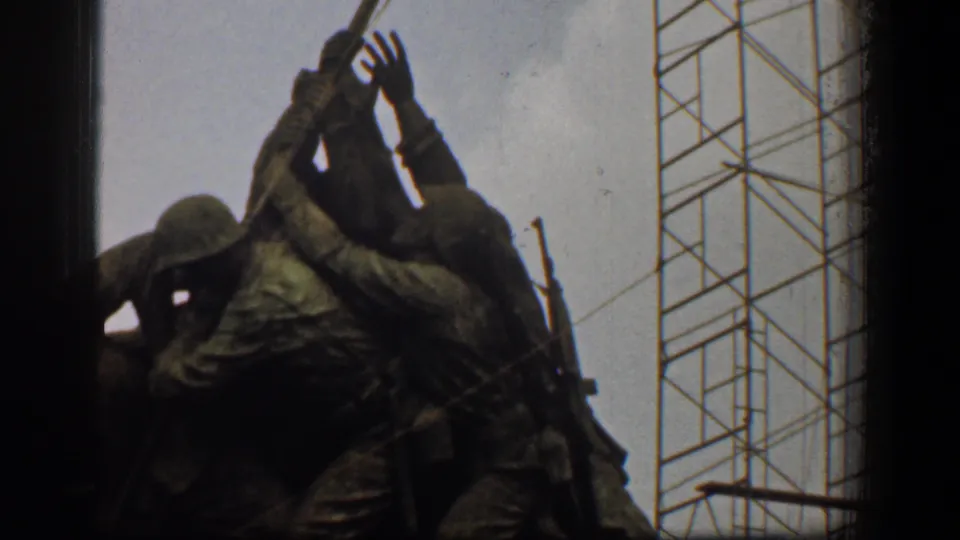 1961 Washington, DC home-movie frame showing the flag-raising war memorial sculpture in soft focus with crane towers and dark film-edge framing.