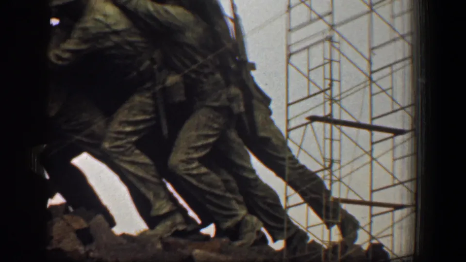 1961 8mm frame of the Marine Corps War Memorial figures from below, with scaffolding lines crossing the background.