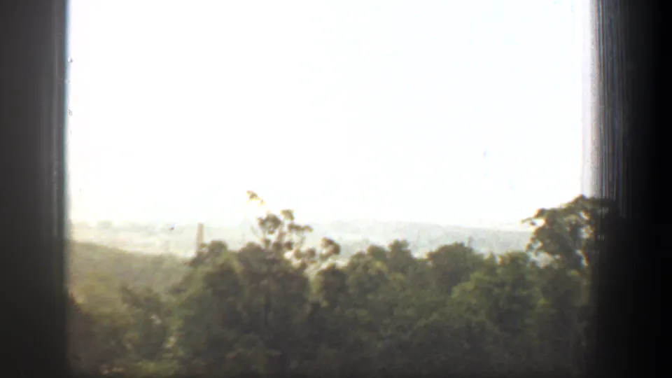 1961 8mm Washington, DC home-movie frame showing treetops and distant haze through a dark window frame.