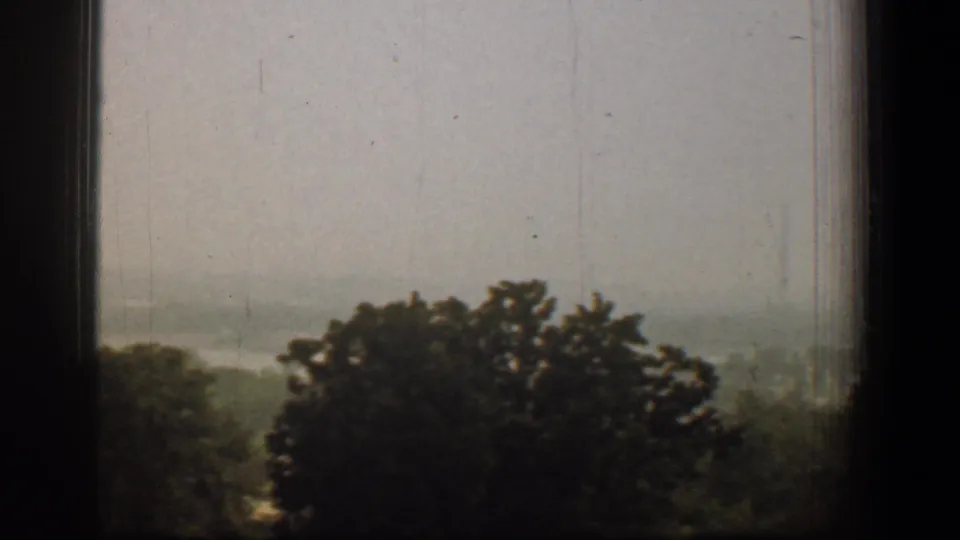 Late frame of the 1961 Washington, DC 8mm pan showing treetops, haze, and faint distant terrain through a window.