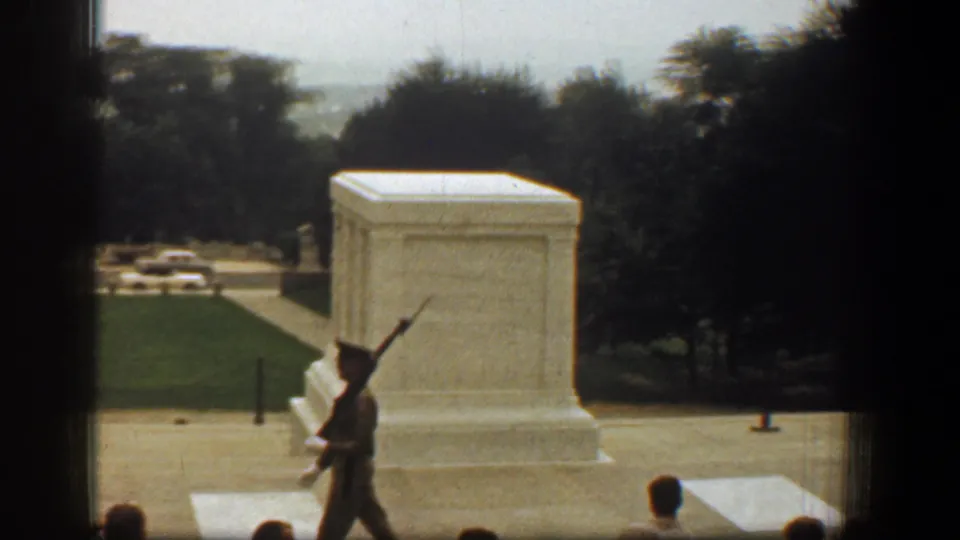 Uniformed soldier with rifle moves in front of the white marble tomb in a Washington, DC memorial setting.