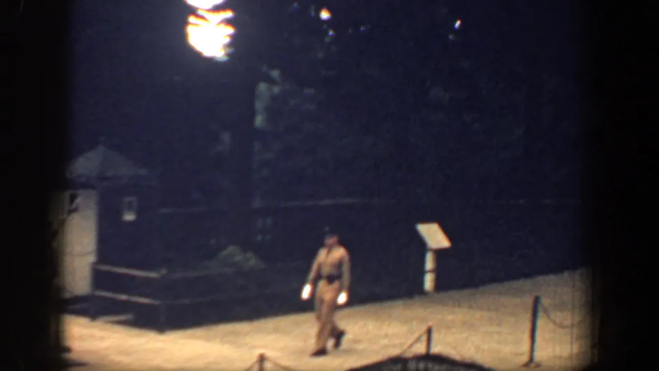 Nighttime 8mm view of a uniformed guard walking near a sentry booth at the memorial site.
