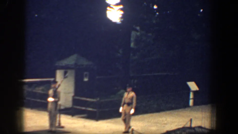 Nighttime memorial guard scene with one soldier at attention and another walking near a sentry booth.