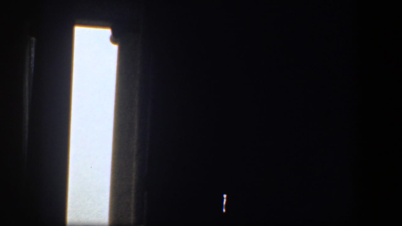 Dark interior window view with a bright vertical opening and small exterior glimpse.