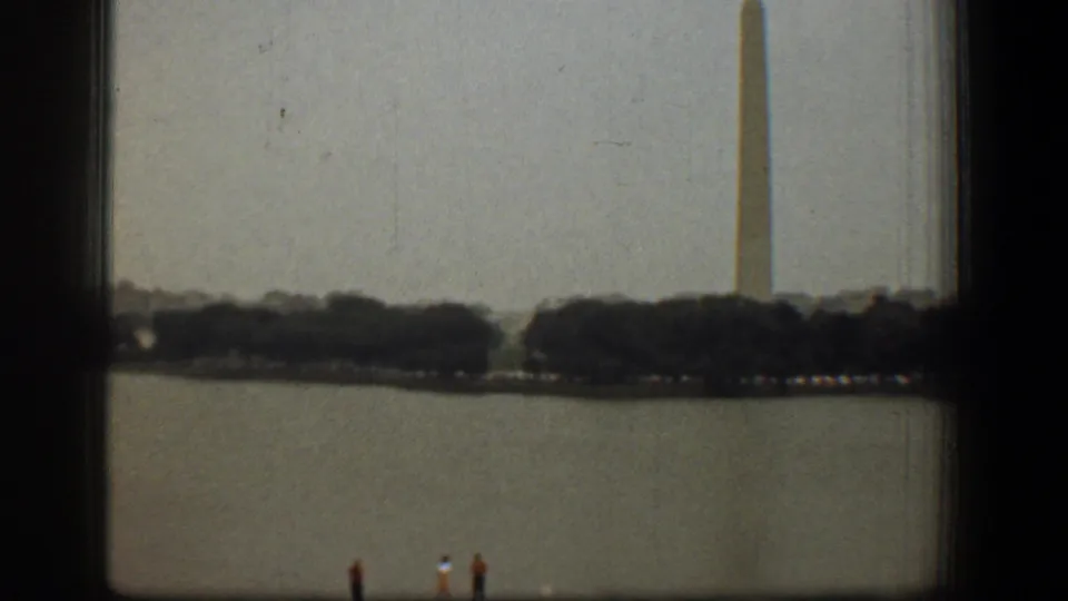A hazy 1961 view across the Reflecting Pool toward the Washington Monument, with distant visitors near the water and window framing in the foreground.