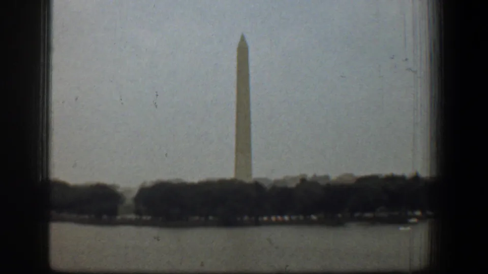 1961 Washington DC frame showing the Washington Monument above a dark tree line, with the Reflecting Pool in the foreground and window edge at left.