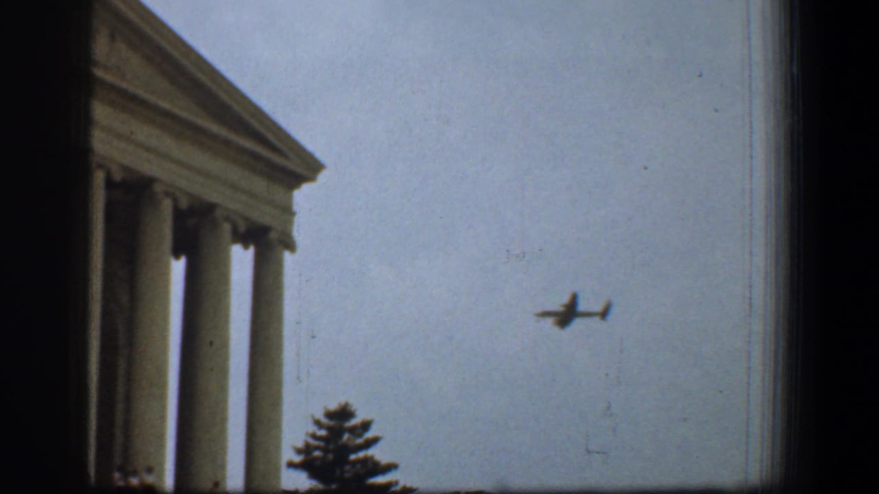 Supreme Court columns at frame edge with a small airplane in the sky.