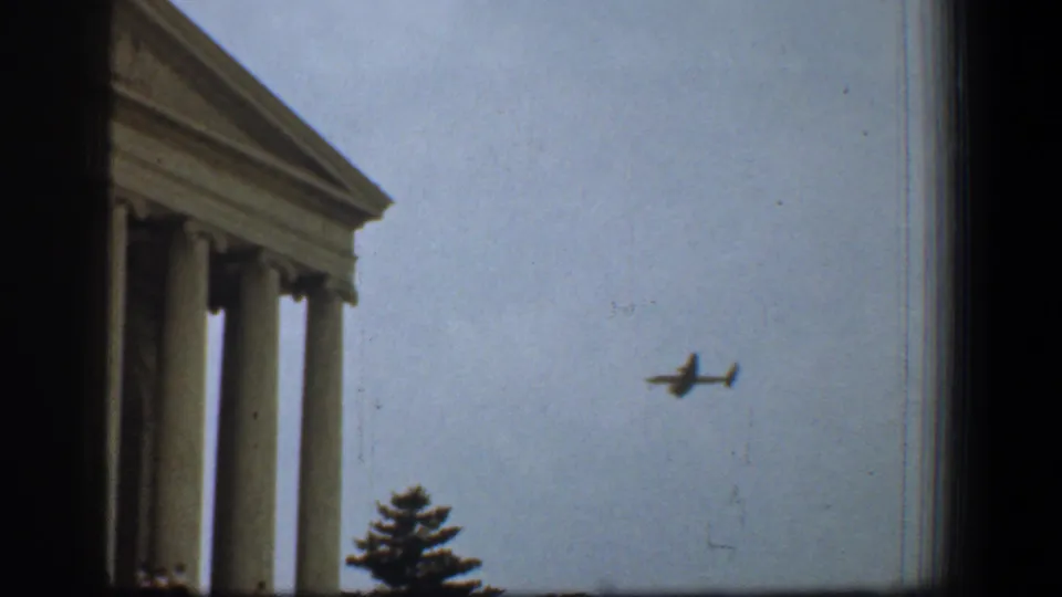 1961 Washington, DC view of the Supreme Court facade edge as a small airplane passes through the sky.