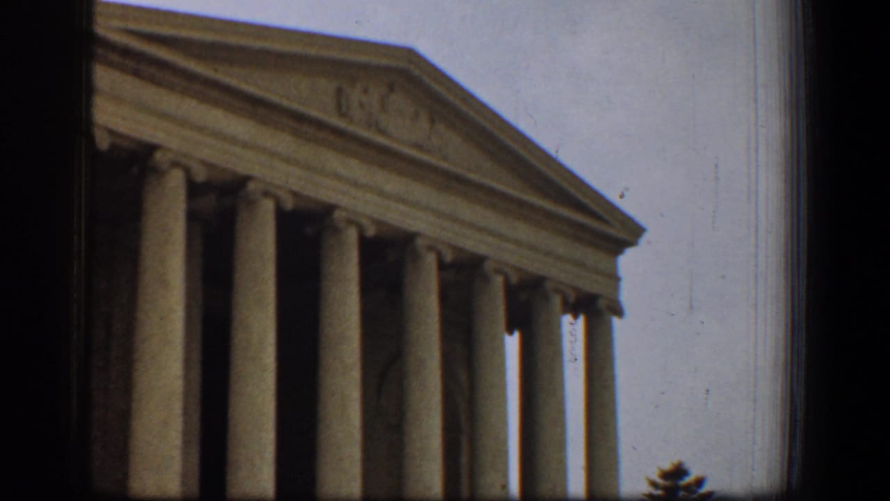 1961 8mm frame of the Jefferson Memorial in Washington, DC, showing columns, pediment, cloudy sky, and dark film edges.