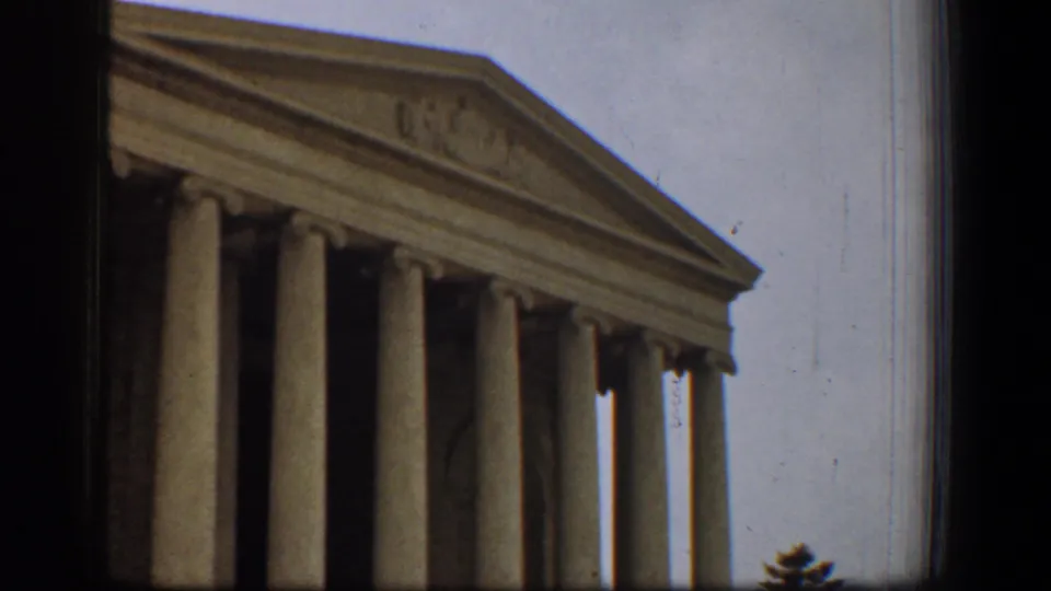 1961 8mm frame of the Jefferson Memorial in Washington, DC, showing columns, pediment, cloudy sky, and dark film edges.