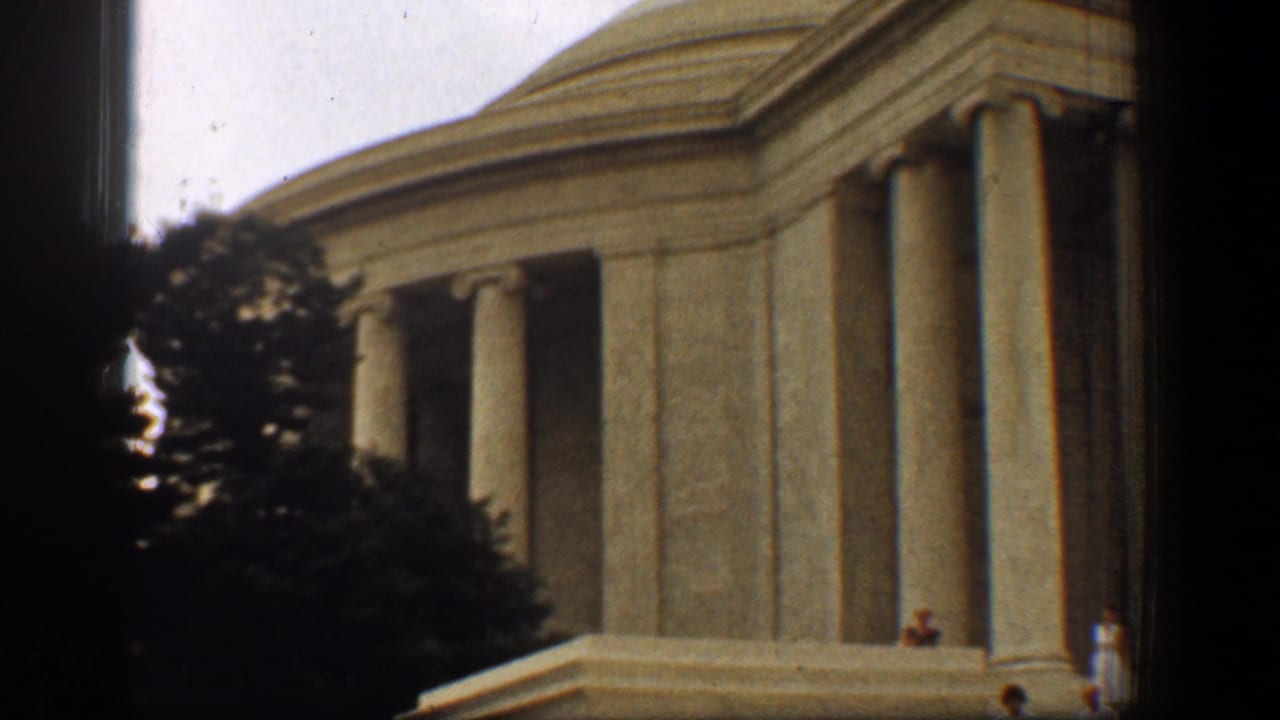 1961 8mm frame of the Jefferson Memorial in Washington, DC, with columns, trees, dark borders, and tiny visitors at the base.