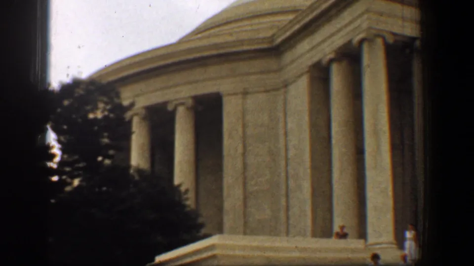 1961 8mm frame of the Jefferson Memorial in Washington, DC, with columns, trees, dark borders, and tiny visitors at the base.