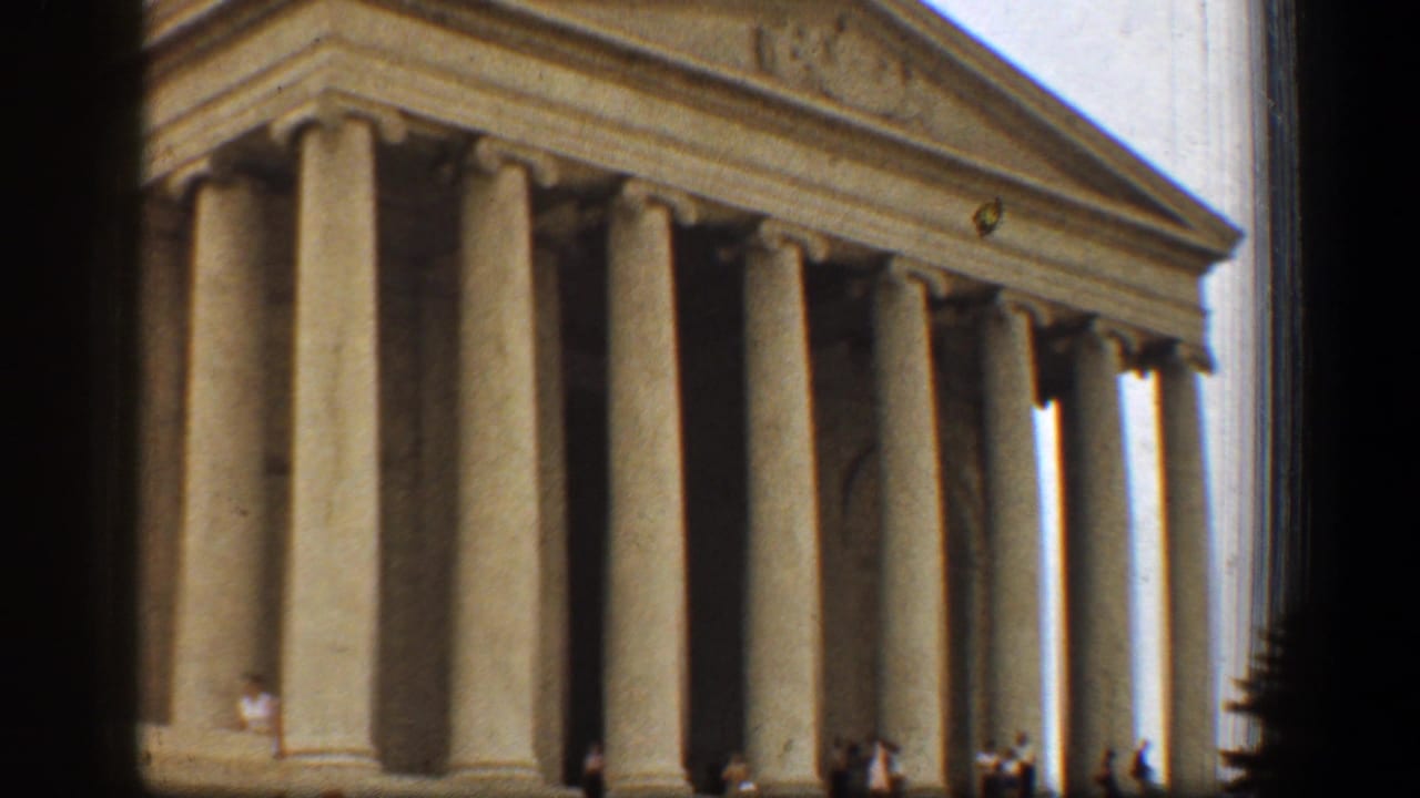 The Lincoln Memorial fills the frame, with tall stone columns, triangular pediment, bright sky, and distant visitors at the base.