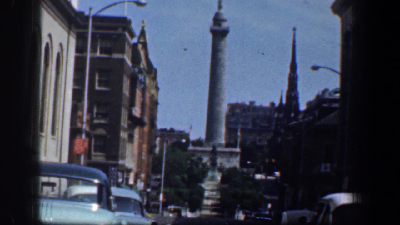 1961 Washington, DC downtown traffic scene with a tall monument, church steeple, masonry buildings, streetlamps, and period automobiles.