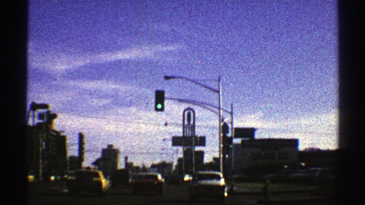 1969 Nevada 8mm frame showing cars on an urban street beneath a green traffic signal, with tall buildings and street signs beyond.