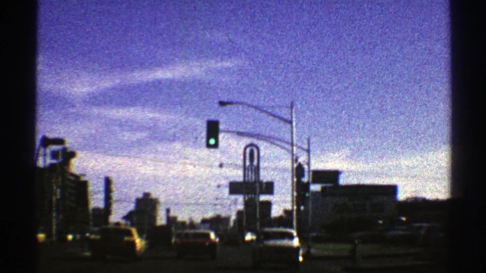 1969 Nevada 8mm frame showing cars on an urban street beneath a green traffic signal, with tall buildings and street signs beyond.