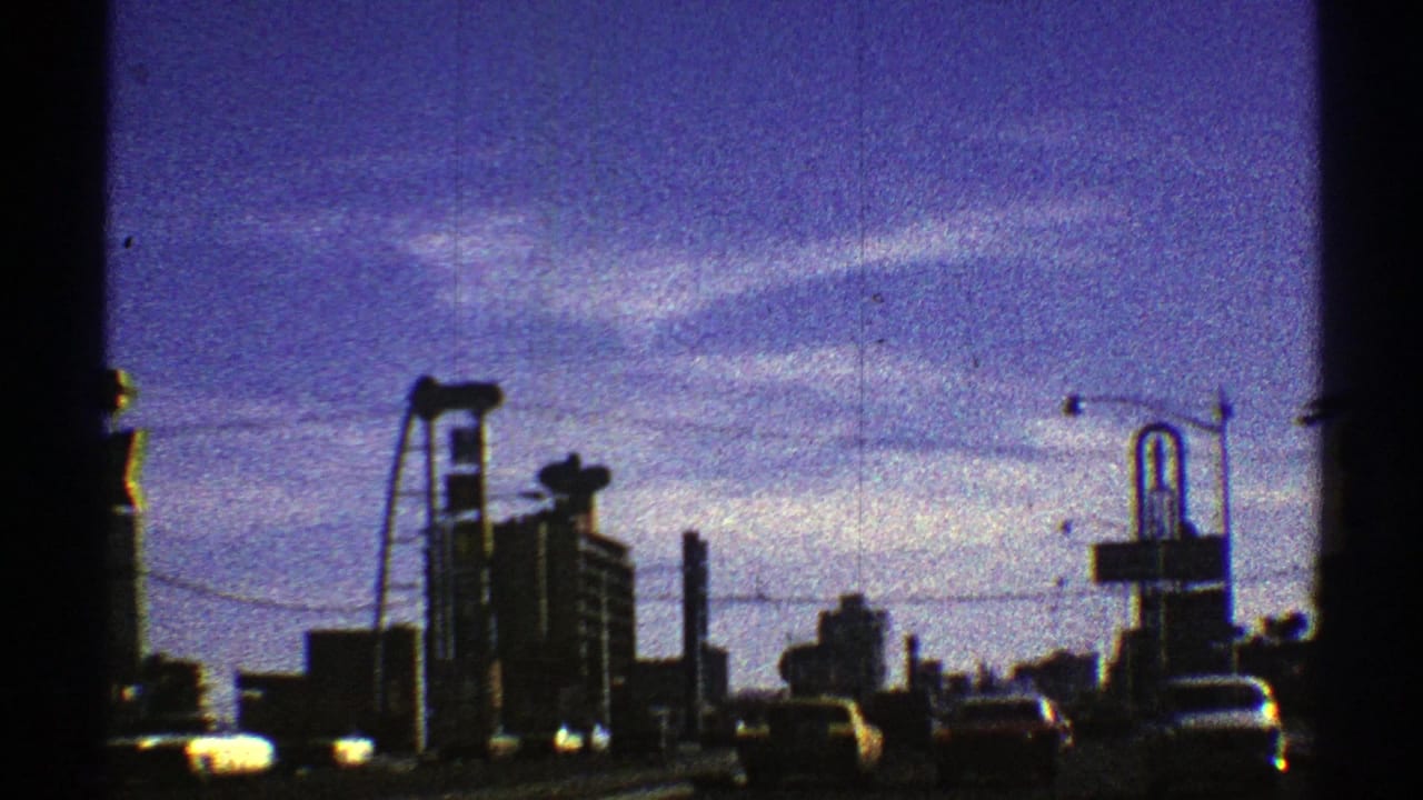 1969 Nevada urban driving frame with cars, tall buildings, a roadside sign structure, utility lines, and visible 8mm frame edge.