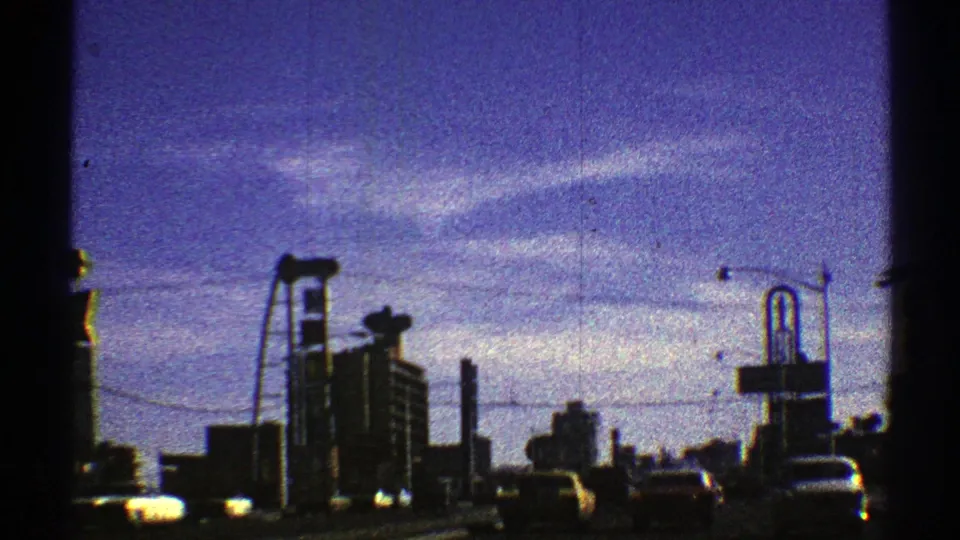 1969 Nevada urban driving frame with cars, tall buildings, a roadside sign structure, utility lines, and visible 8mm frame edge.