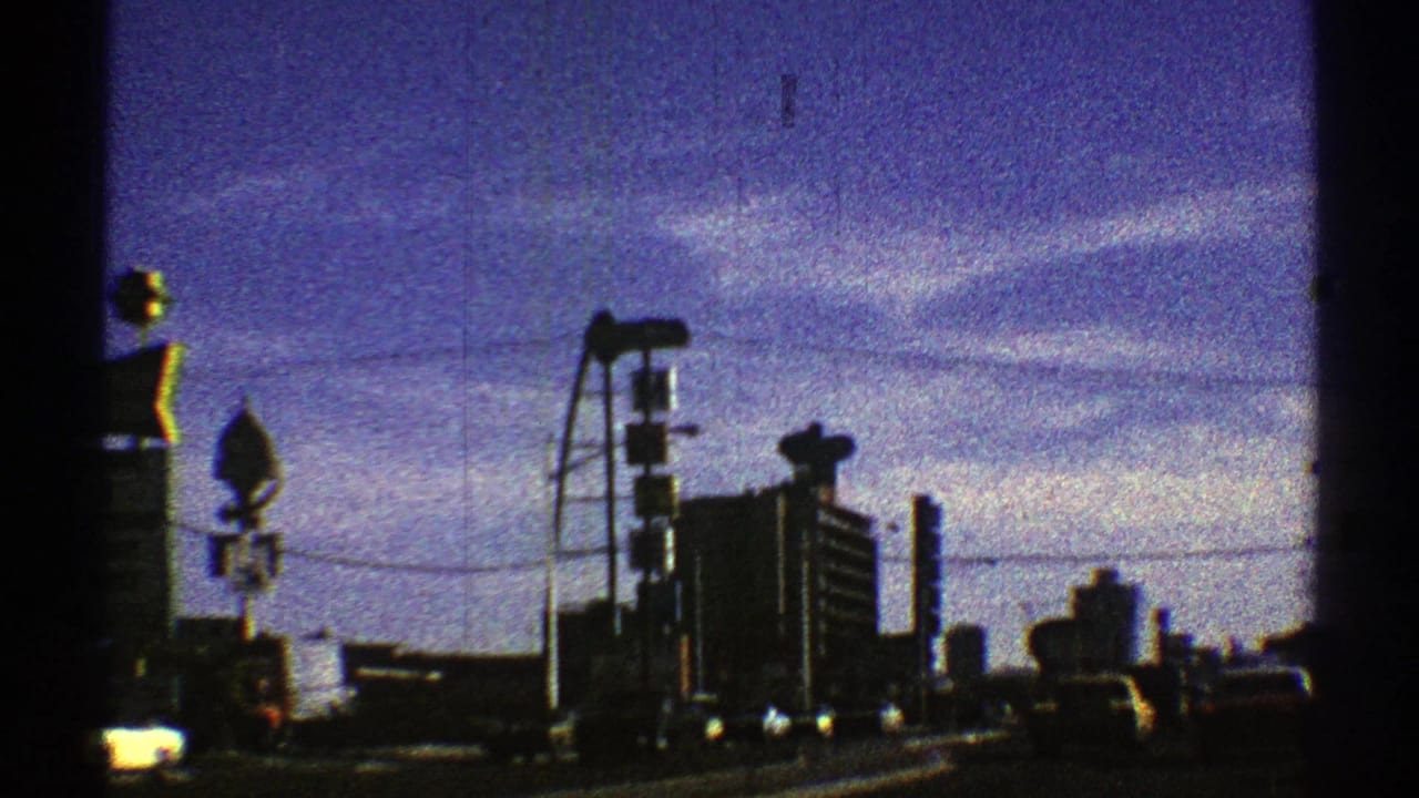 Late clip frame from 1969 Nevada showing urban traffic, tall building forms, street signs, and utility lines under a purple-blue sky.