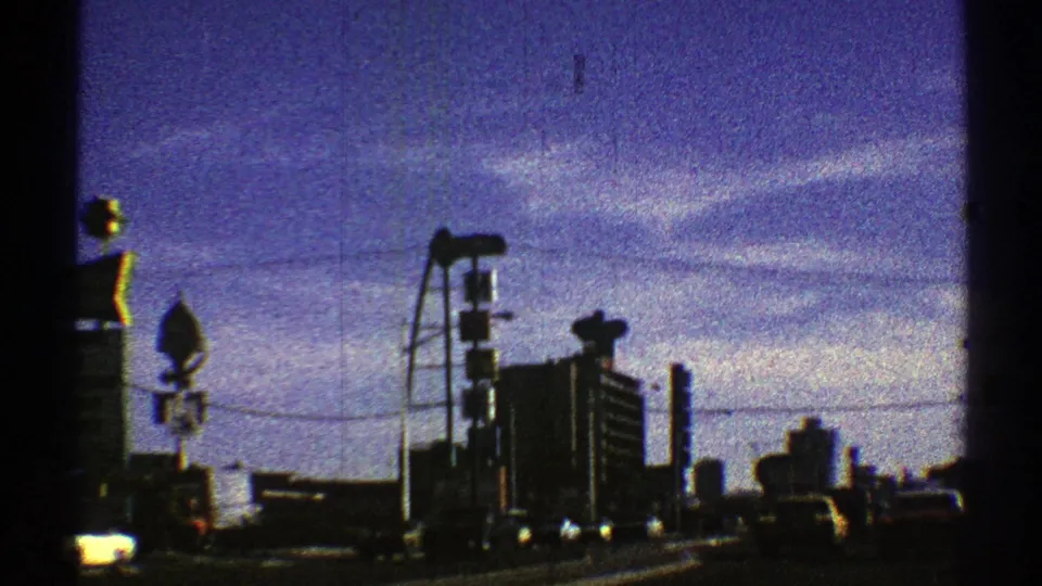 Late clip frame from 1969 Nevada showing urban traffic, tall building forms, street signs, and utility lines under a purple-blue sky.