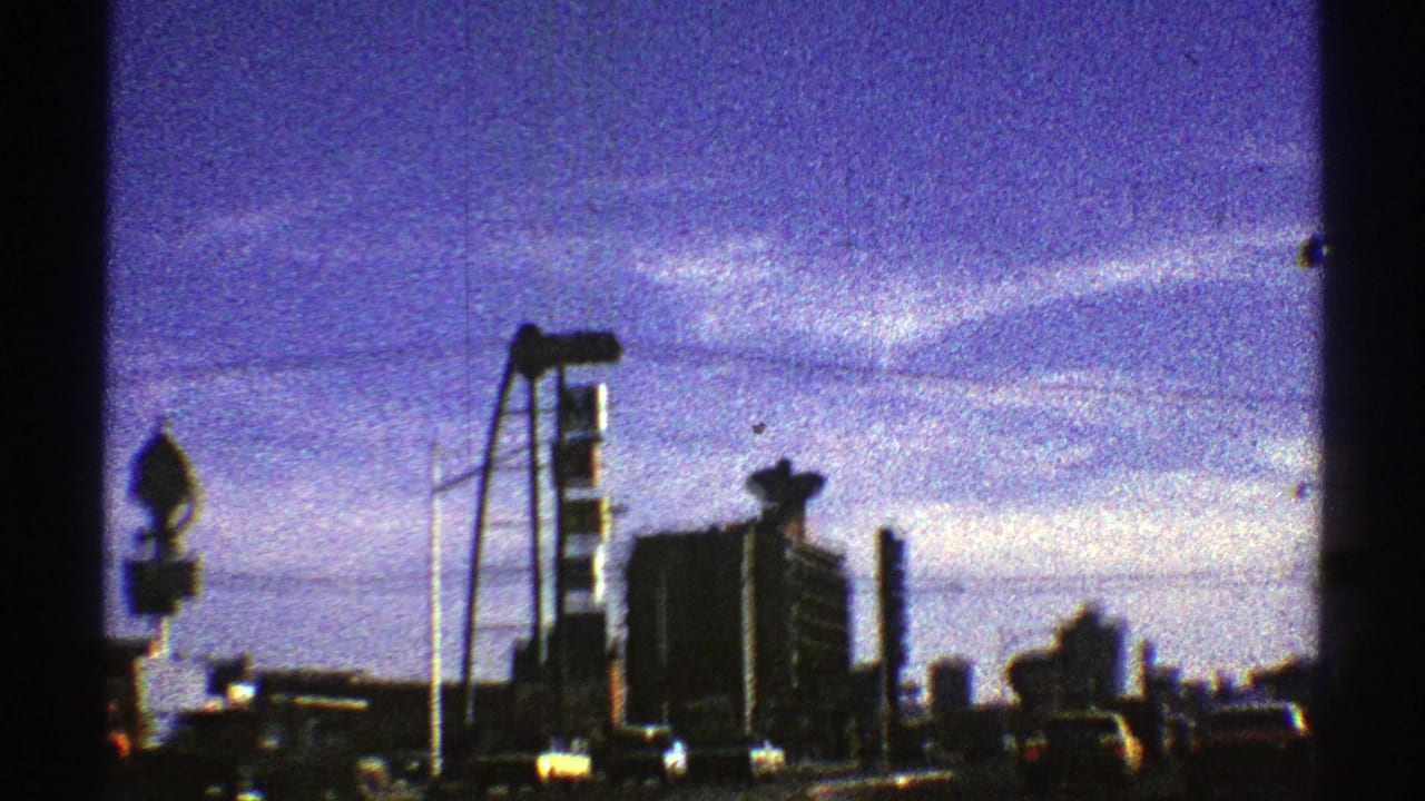1969 Nevada road view approaching a Shell gas station area, with tall signage, streetlights, cars, and a vivid blue-purple sky.