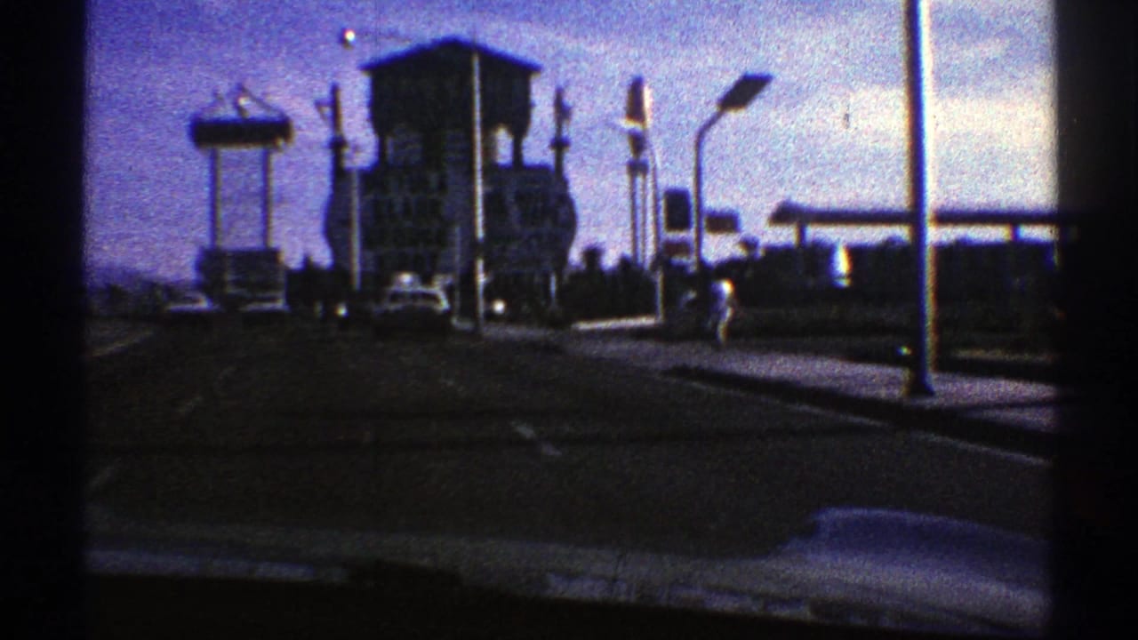1969 Nevada windshield view showing roadside signs, a billboard, streetlights, and period cars near a gas station approach.
