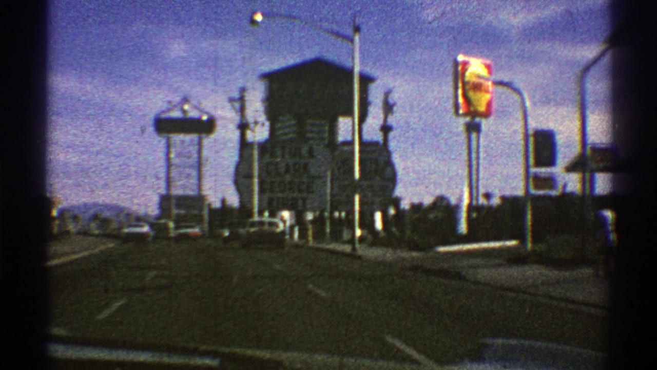 Nevada road scene with a red and yellow Shell sign, large entertainment billboard, streetlights, and approaching traffic in 8mm footage.