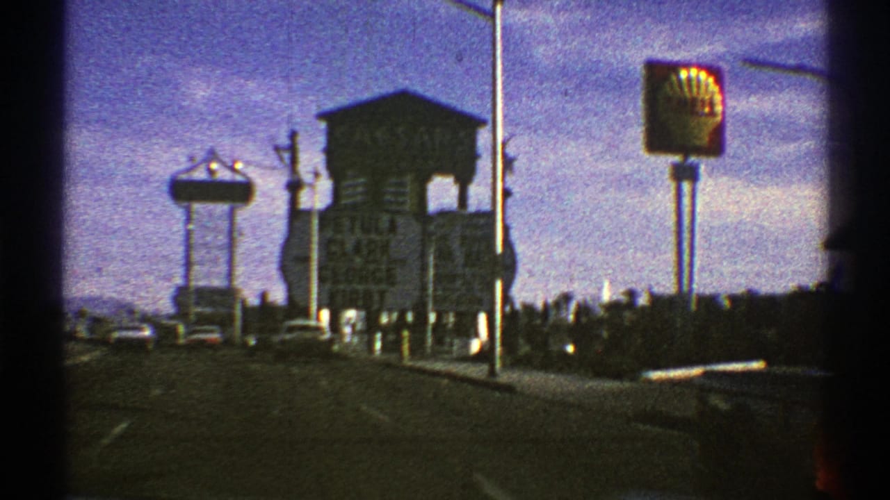 Roadside city view with Shell sign, traffic lights, poles, cars, and a water-tower-like structure.