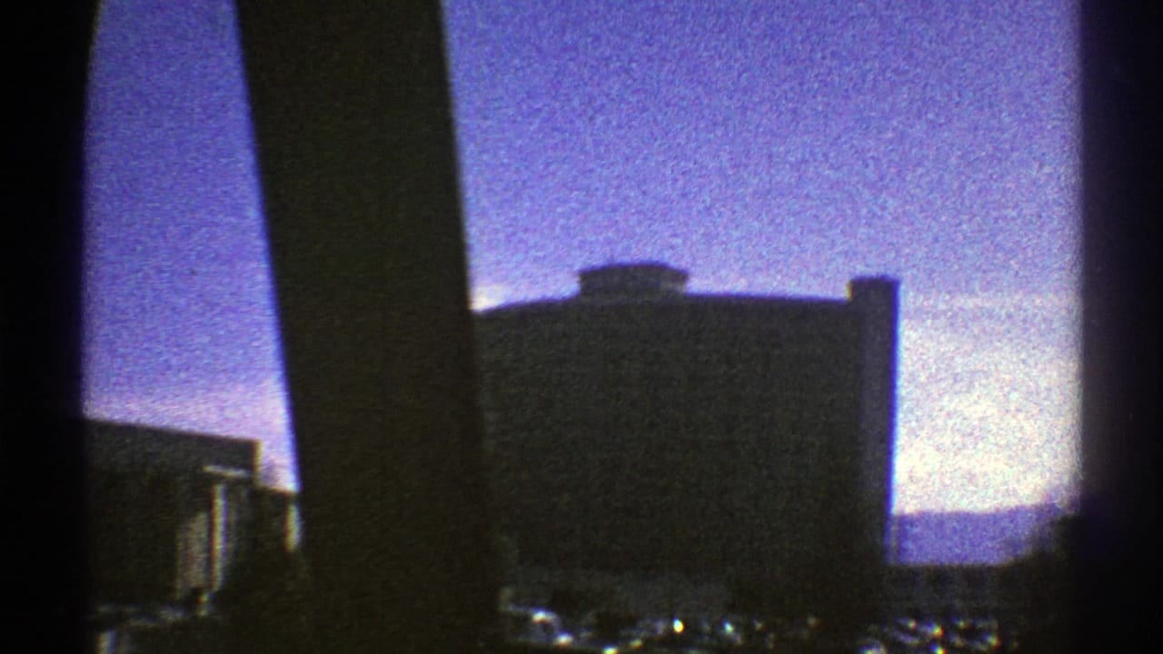 A large modern building and parked cars in a Nevada city are seen through dark vehicle or window supports in 1969 footage.