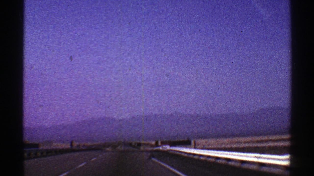 Nevada highway view from a moving car, with bright guardrail, low mountains, and hazy purple 8mm sky.