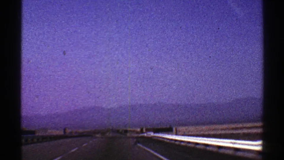 Nevada highway view from a moving car, with bright guardrail, low mountains, and hazy purple 8mm sky.