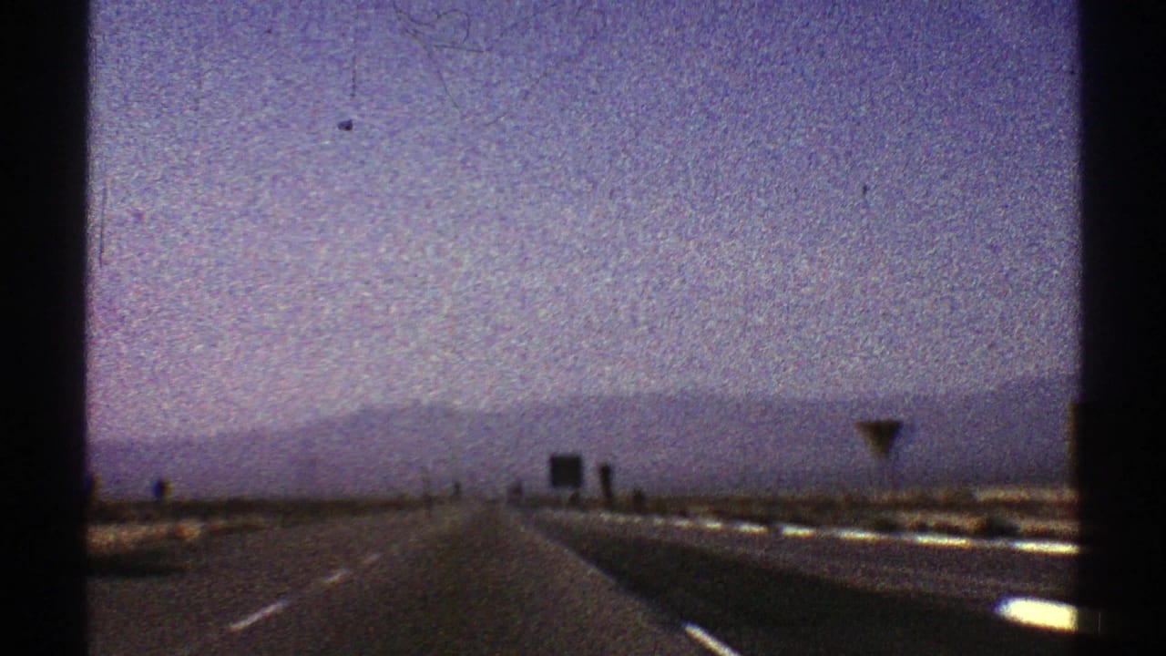 Straight highway receding toward distant mountains with roadside signs on the right.