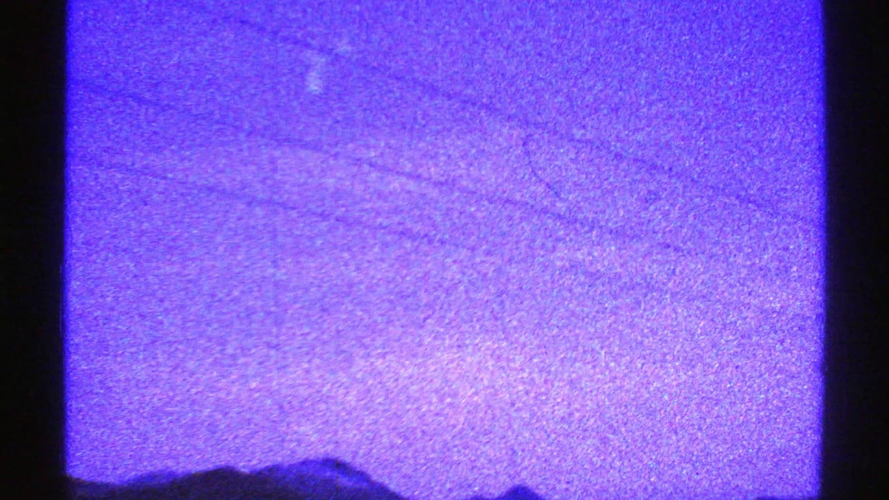 A mostly purple 8mm frame with visible film grain and faint desert-mountain forms near the lower edge.