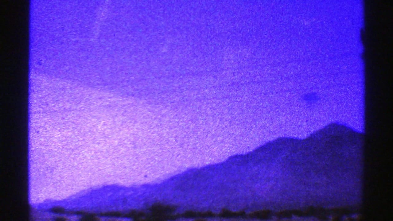 Blue-tinted mountain ridge under a bright sky with dark vertical film borders.